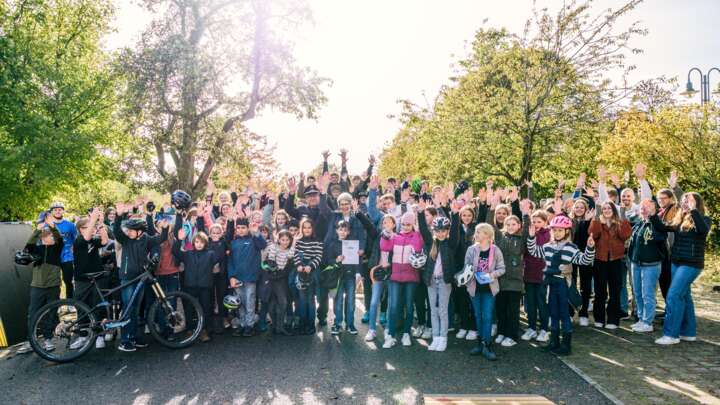 Ein Gruppenfoto von Kindern mit erhobenen Armen. Vorne links ist ein Fahrrad zu sehen.